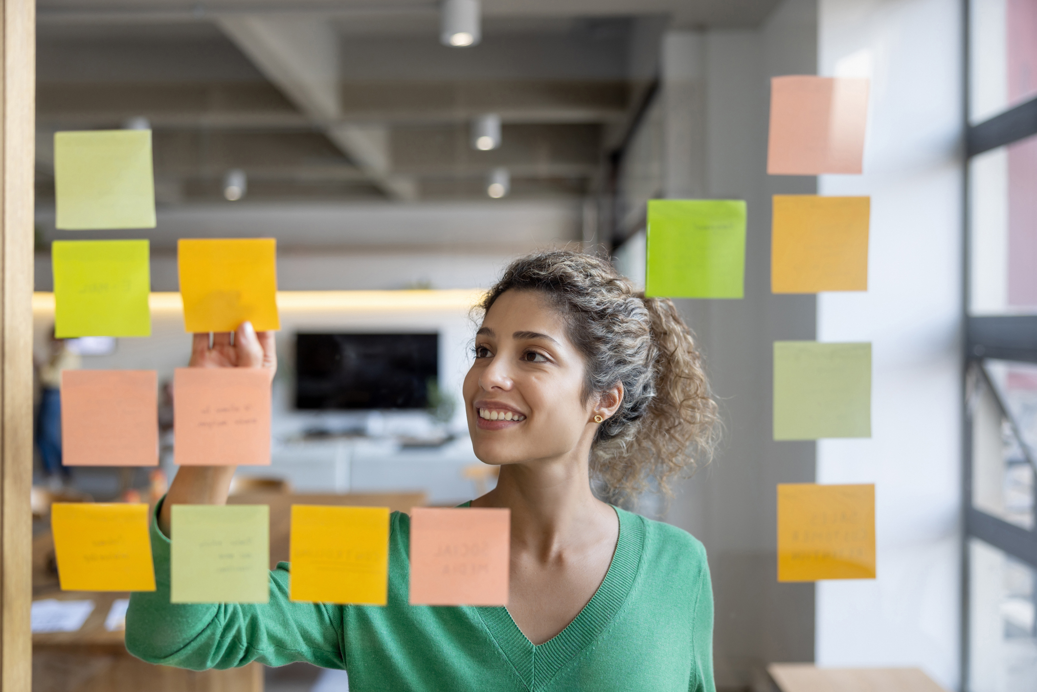 Happy Latin American female entrepreneur brainstorming at the office and organizing ideas on adhesive notes